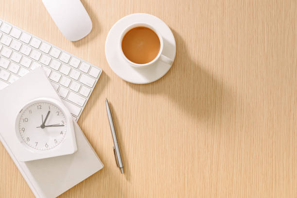 istock Modern white office desk with keyboard, mouse, clock, book, pen and cup of coffee. Top view with copyspace. Business and strategy concept mockup. 1132900357