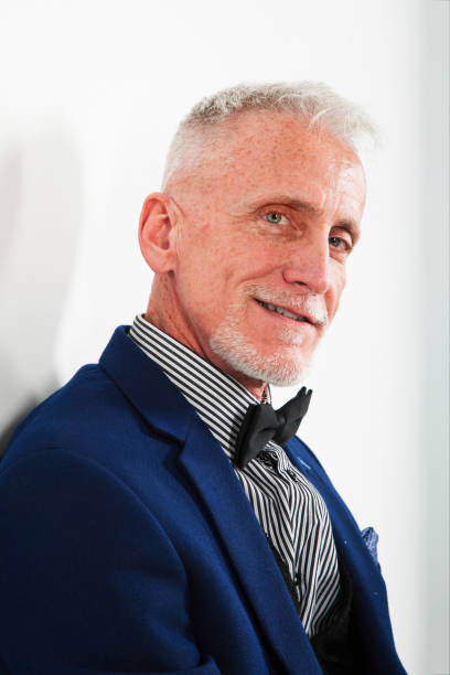 istock Mature man smiling portrait in blue suit on gray background back lit 1132900967