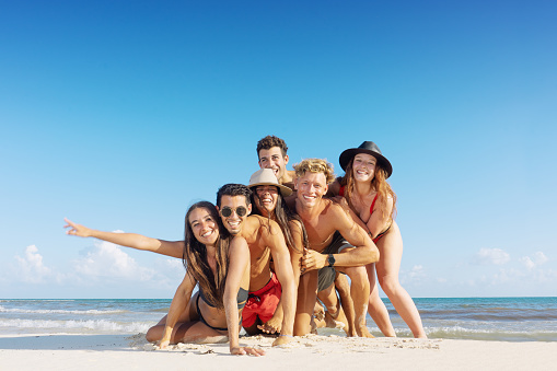 Group of friends standing together on the beach having fun and enjoying their summer vacation