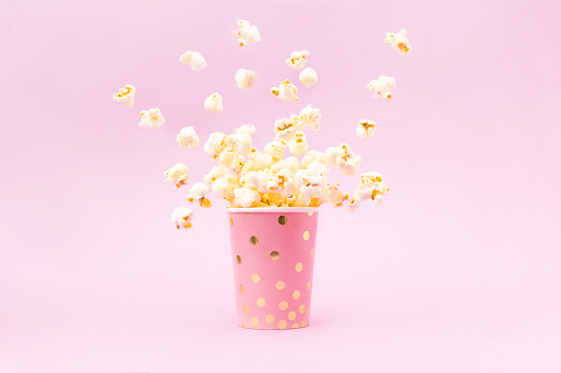 Flying Popcorn in a bright glass and on a pink background. Copy space