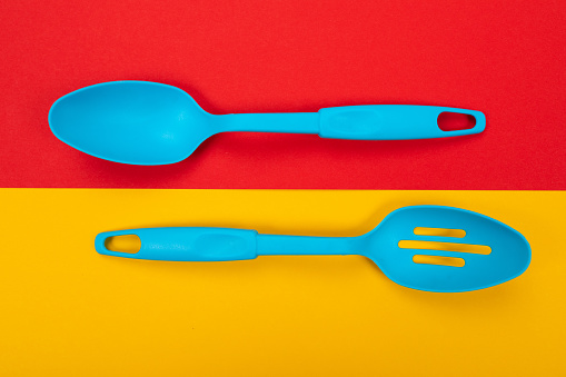 two large plastic blue kitchen spoons lie parallel to each other on a yellow-red background. Can be used as a background in the food industry. Stylish menu design for the restaurant