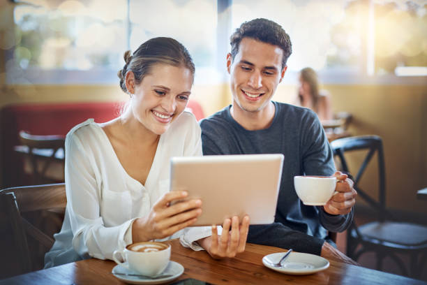 istock Young couple in cafe laughing at digital tablet image together 1132921154