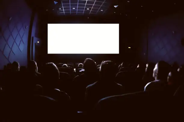Photo of People in the cinema watching a movie. Blank empty white screen