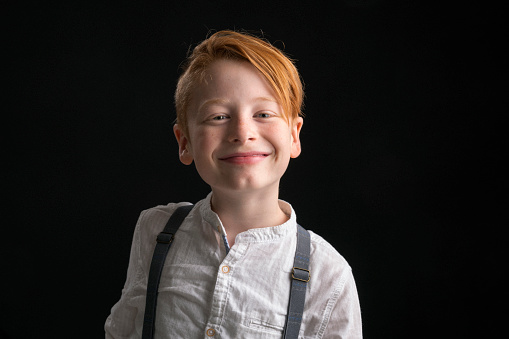 Close-up of smiling little boy. Portrait of cute happy kid against black background. He is wearing casuals in studio.