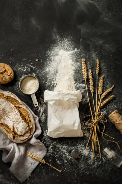 Bread, flour bag, wheat and measuring cup on black