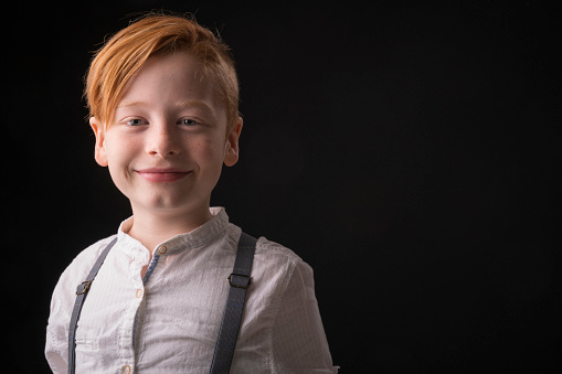 Portrait of smiling little boy wearing suspenders. Close-up of male kid against black background. He is in casuals.