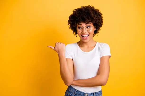 Photo of Portrait of nice cute smart clever attractive beautiful cheerful glad positive wavy-haired lady pointing aside ad advert copy empty blank space isolated over bright vivid shine yellow background