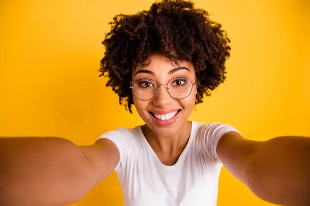 Close up photo beautiful amazing she her dark skin lady make take selfies cute attractive white teeth gorgeous smile wear specs casual white t-shirt isolated yellow bright vibrant vivid background.