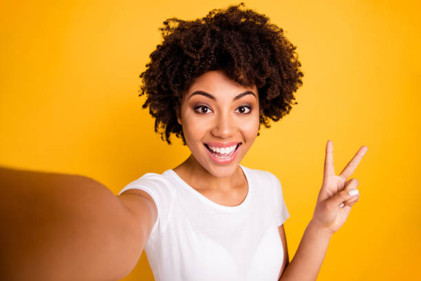 cerrar foto hermosa increíble ella su piel oscura señora brazo mano mostrar v-sign hacer tomar selfies lindo atractivo blanco dientes desgaste casual blanco camiseta aislado amarillo brillante vibrante fondo vivo - video conference camera fotografías e imágenes de stock