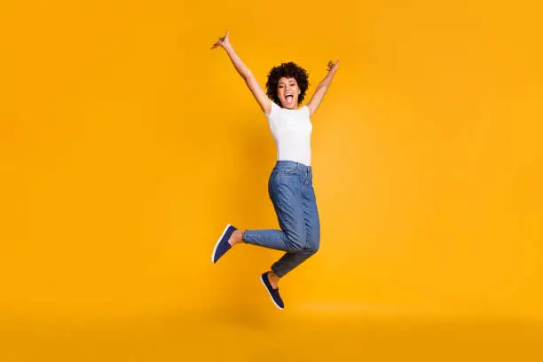 Full length body size side profile photo jumping high beautiful she her lady hands arms up win game play match wearing casual jeans denim white t-shirt clothes isolated yellow bright vivid background.