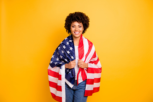 Close up photo beautiful amazing she her dark skin lady hands arms hold american flag best country party 4th of july wearing casual jeans denim white t-shirt isolated yellow bright vibrant background.