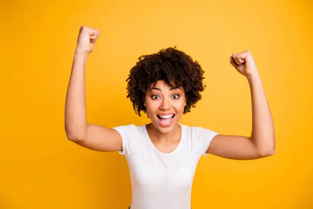 Close up photo beautiful amazing she her dark skin lady not believe yelling glad hands arms fists raised great big win competition wear casual white t-shirt isolated yellow bright vibrant background.