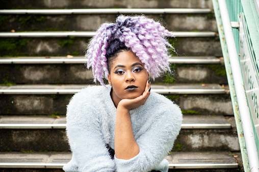 Outdoor portrait of a young woman with purple coloured hair standing outside.