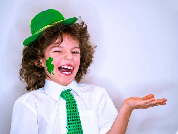 istock Curly child boy having fun during Saint Patrick celebrations over a light background. I'm smiling boy with a green shamrock on my cheek holding an imaginary subject in my hand. Copy space 1132936852
