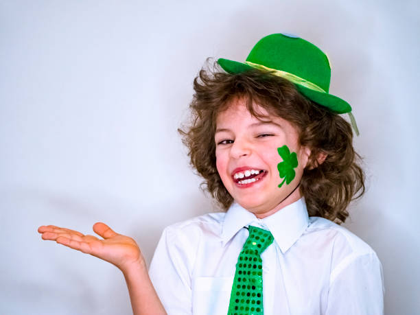 istock Curly child boy having fun during Saint Patrick celebrations over a light background. I'm smiling boy with a green shamrock on my cheek holding an imaginary subject in my hand. Copy space 1132936872
