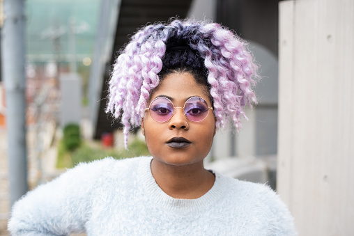 Outdoor portrait of a young woman with purple coloured hair standing outside.