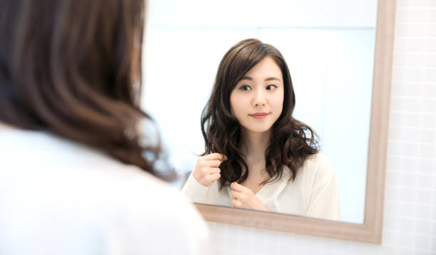 若いアジアの女性は、鏡を見ています。 - スタイリング ストックフォトと画像