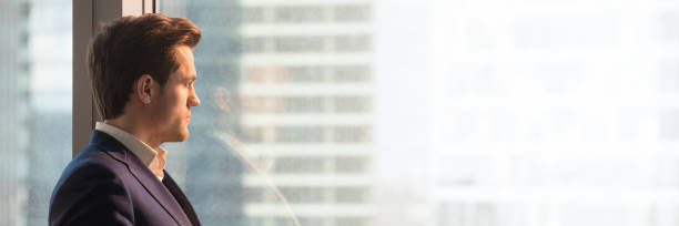 istock Panoramic image businessman in suit looking through office window 1132941029