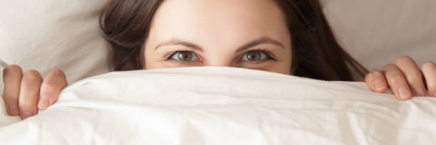 istock Horizontal image woman hiding under white blanket lying on pillow 1132941036