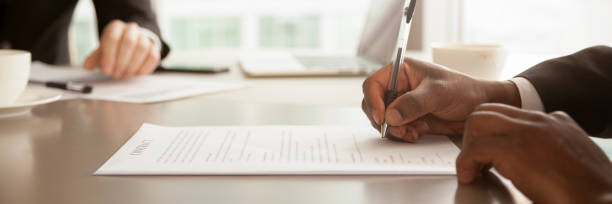 horizontal closeup image black businessman sitting at desk signing contract - document contract law business imagens e fotografias de stock