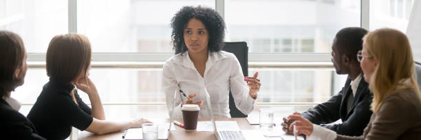 Horizontal photo african female boss talking at corporate meeting Horizontal photo people sitting at boardroom african business woman talking with staff at formal meeting briefing, diverse client partners listens boss ceo team leader banner for website header design narrow photos stock pictures, royalty-free photos & images