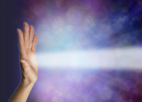 female hand facing out with a beam of white energy streaming out against a blue bokeh energy field background with copy space