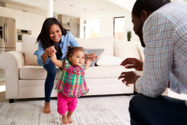 Family At Home Encouraging Baby Daughter To Take First Steps Family At Home Encouraging Baby Daughter To Take First Steps family at home stock pictures, royalty-free photos & images