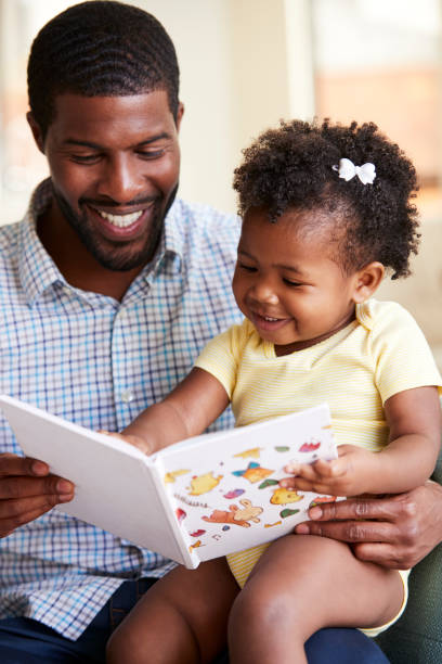 маленькая дочь и отец, сидя на диване чтение книги вместе - child book reading baby стоковые фото и изображения
