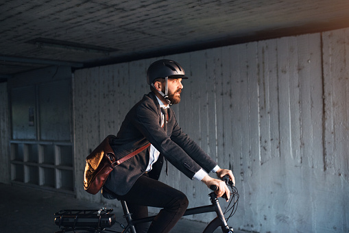 A side view of hipster businessman commuter with electric bicycle traveling to work in city. Copy space.