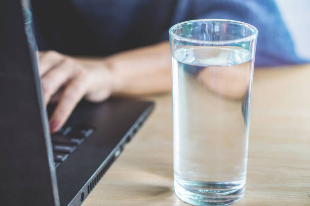 istock woman hand drinking fresh water while working on computer laptop at office 1132953812