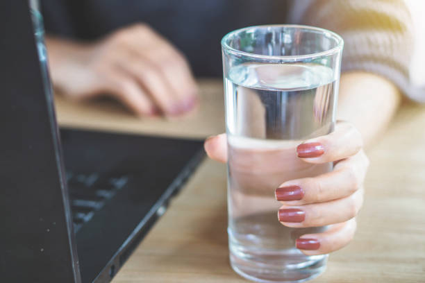 istock woman hand drinking fresh water while working on computer laptop at office 1132953843