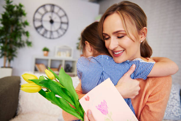 ласковая мама и ее дочь обнимаются дома - mothers day tulip yellow greeting card стоковые фото и изображения