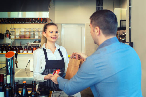 istock Man paying takeaway order by credit card on reader holded by smiling waitress working at shop counter restaurant. Customer using credit card for payment. Young cashier accepting payment over nfc technology 1132959541