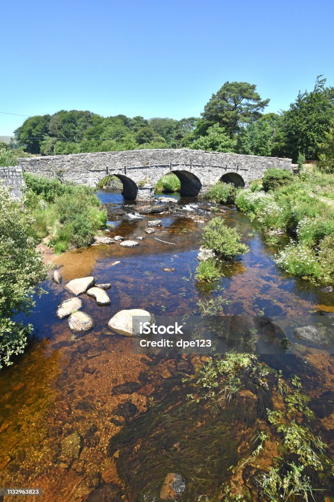 Ancient stone Clapper Bridge, Dartmoor, England An ancient granite clapper bridge over the East Dart river, at Postbridge, Dartmoor National Park, Devon, England. This clapper bridge was built in the 13th centuary for pack horses to carry tin to Tavistock. It is a listed sturcture. Ancient Stock Photo