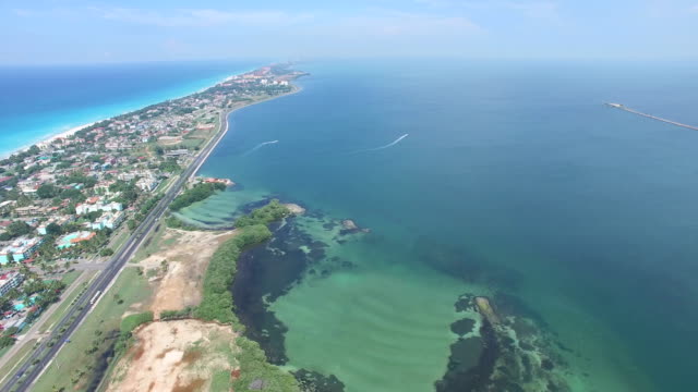 Drone flies over tropical island in the bay of Atlantic Ocean. Bird's-eye view to main road, streets, coastline, houses.