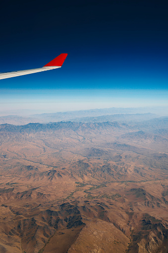Aerial view at mountain range from airplane above Afghanistan. Geological surface structures of planet earth. Horizon over land. No people. Aircraft wing to be seen. XXXL (Sony Alpha 7R)