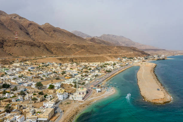 kleine stadt tiwi an der küste des golfs von oman, mit einer gebirgskette dahinter - tiwi stock-fotos und bilder