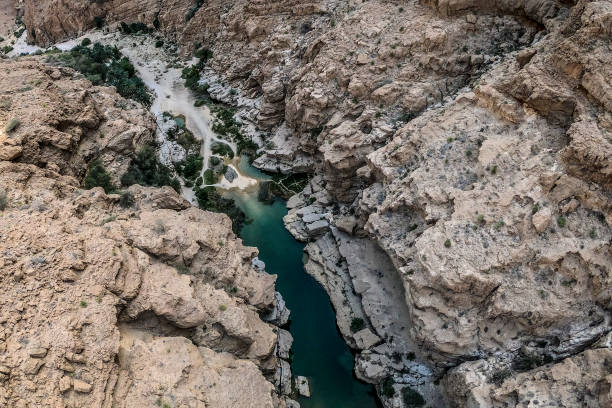 istock Wadi Shab Canyon bed ending with a small emerald-colored body of water, surrounded by sharp rocks 1132969059