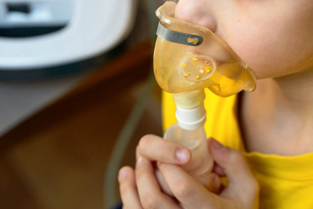 Child makes inhalation at home with nebulizer on out of focus background upper clodeup view Child makes inhalation at home with nebulizer on out of focus background. Example of combating respiratory diseases such as tracheitis bronchitis pneumonia with medical equipment at home conditions. pediatric nebulizer mask stock pictures, royalty-free photos & images