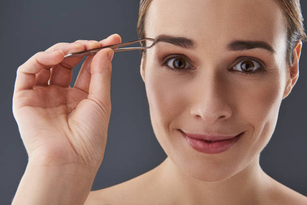 istock Pretty lady with tweezer in hands looking at camera 1132969869