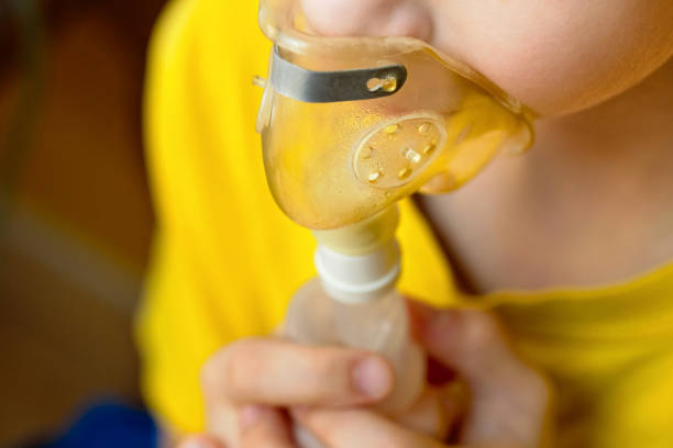 Child closeup makes inhalation at home with nebulizer on out of focus background. Child makes inhalation at home with nebulizer on out of focus background. Example of combating respiratory diseases such as tracheitis bronchitis pneumonia with medical equipment at home conditions. pediatric nebulizer mask stock pictures, royalty-free photos & images