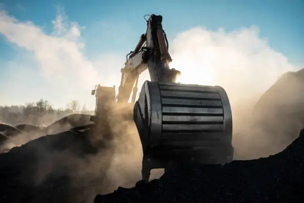 Photo of Yellow big excavator in the coal mine, loads the breed, with the bright sun and nice blue sky in the background. Mining truck mining machinery. Technique in coal mine