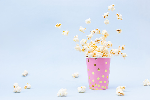 Flying Popcorn in a bright glass and on a blue background. Copy space