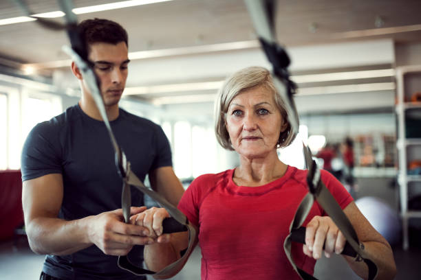 istock A senior woman in gym with a young trainer doing exercise with TRX. 1132975988