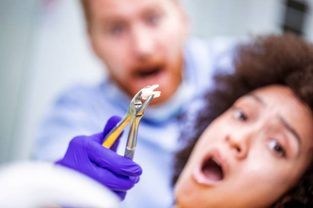 Close-up view of dental nippers gripping an extracted tooth. A doctor and a patient are in the back.