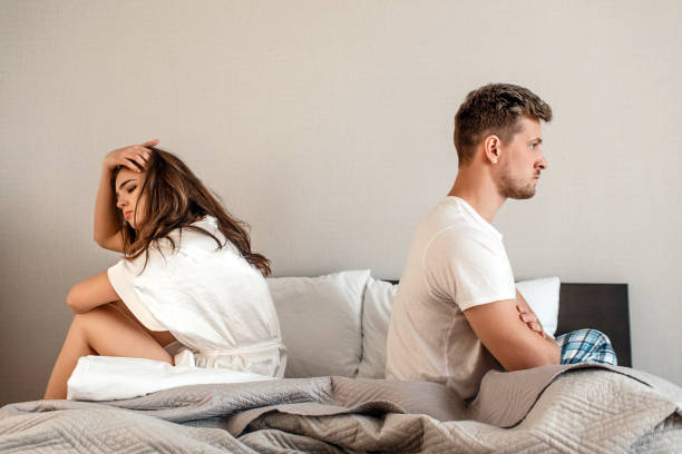 jeunes couples dans la chambre. homme et femme malheureux sont assis dos à dos dans le lit, scène de maison de querelle de couple - domestic life sadness family bed photos et images de collection