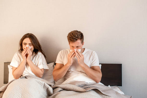 giovane coppia nel letto. uomo e donna malati soffiano nasi e soffrono di malati in camera da letto - cold and flu flu virus bed couple foto e immagini stock