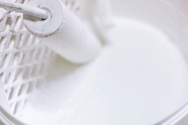 Paint roller hanging on inside of paint box full with white paint
