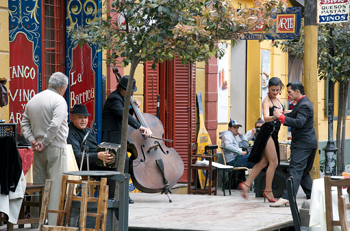 Buenos Aires, Argentina - October 25, 2011: Musicians performe the tango, while a young couple dance the tango in front of a restaurant. La Boca is the best place to watch these performances when visiting Buenos Aires.