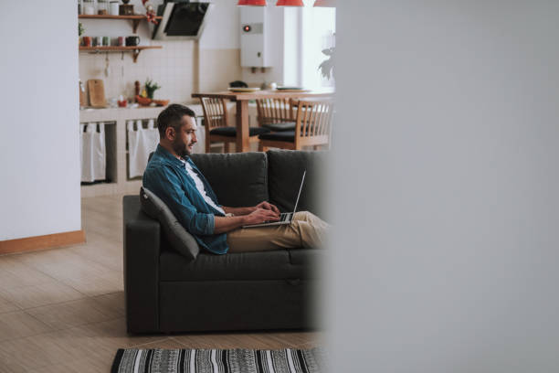 istock Handsome young man in casual clothing using modern laptop at home 1132987166